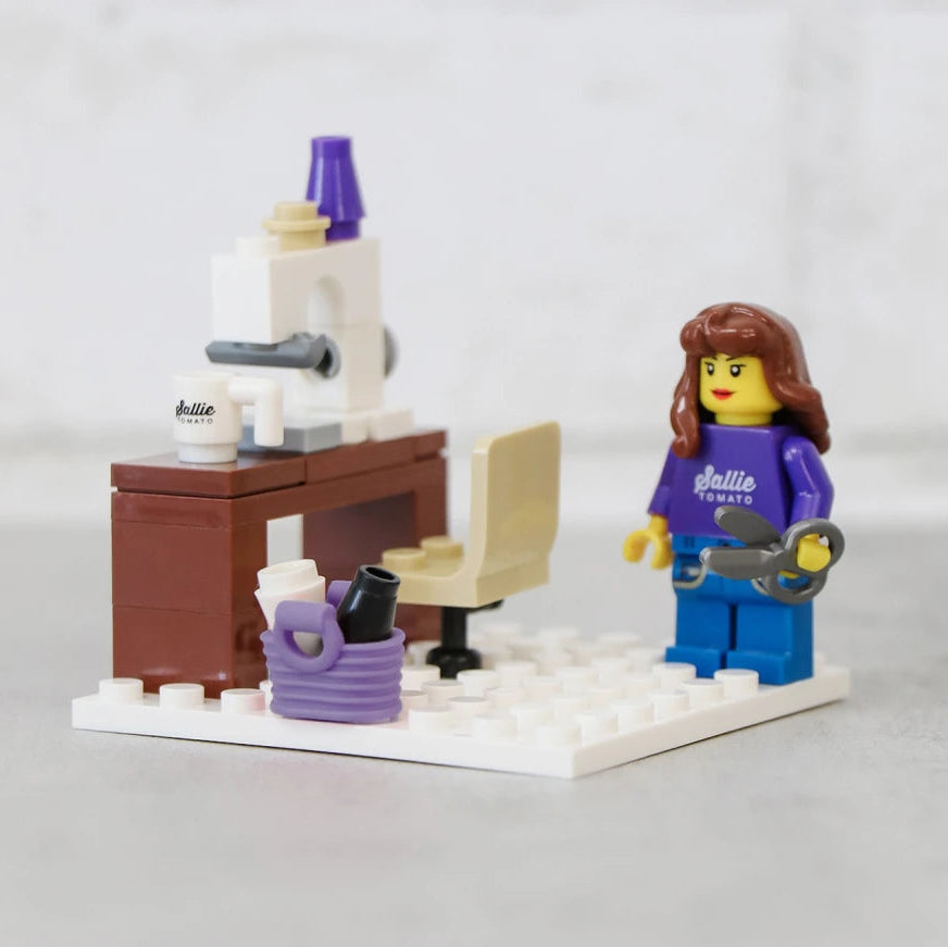 Stitch up creativity — brick-by-brick! The Sallie Tomato Sewist Building Block Set brings your sewing studio to life in miniature form. Perfect for makers, collectors, and sewing enthusiasts, this adorable build includes a sewing machine station, a comfy studio chair, and a cheerful sewist minifigure ready to create with jumbo scissors in hand.